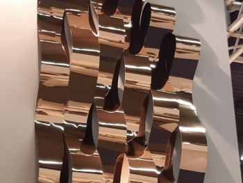 Installation murale architecturale avec des bandes de miroir flexible chromé en bronze, créant un effet ondulé et lumineux.
